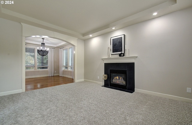 unfurnished living room featuring carpet flooring, a tray ceiling, and a notable chandelier