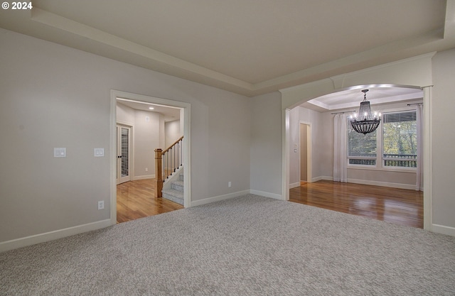 empty room with hardwood / wood-style floors, a tray ceiling, and an inviting chandelier