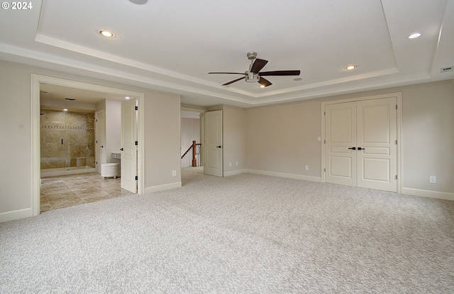 unfurnished bedroom featuring ensuite bath, a tray ceiling, and light carpet