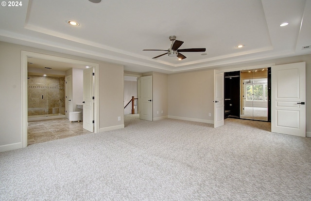 unfurnished bedroom featuring light carpet, ensuite bathroom, and a raised ceiling