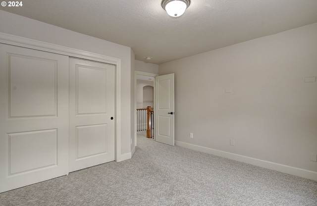 unfurnished bedroom featuring a closet, light carpet, and a textured ceiling