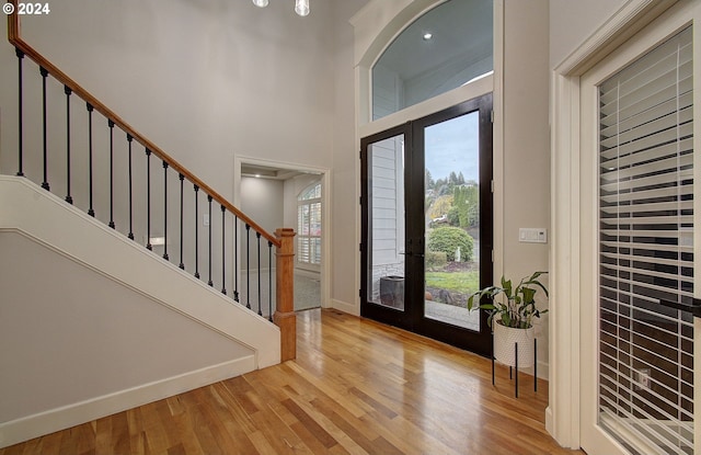 foyer featuring french doors, a towering ceiling, and light wood-type flooring