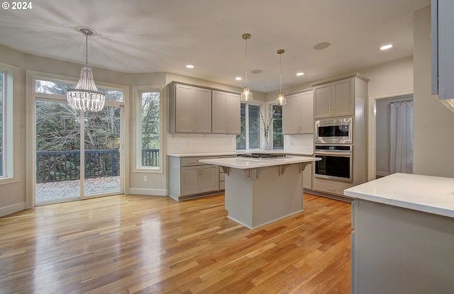 kitchen featuring gray cabinets, hanging light fixtures, light wood-type flooring, and appliances with stainless steel finishes