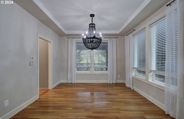 unfurnished dining area featuring a notable chandelier, a raised ceiling, and light wood-type flooring