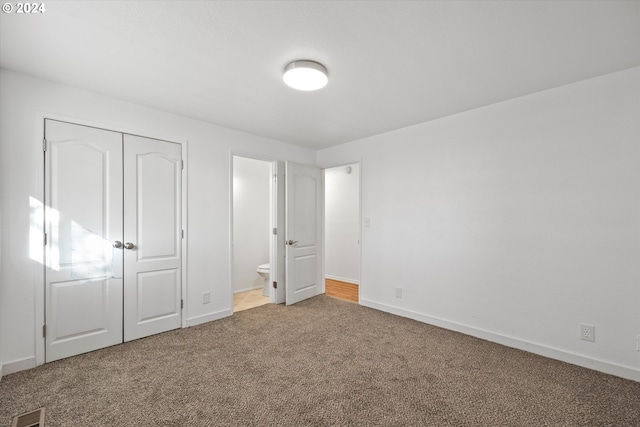 unfurnished bedroom with ensuite bath, a closet, and carpet floors