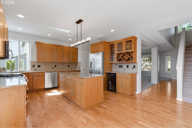 kitchen with beverage cooler, a kitchen island, pendant lighting, light hardwood / wood-style floors, and stainless steel appliances