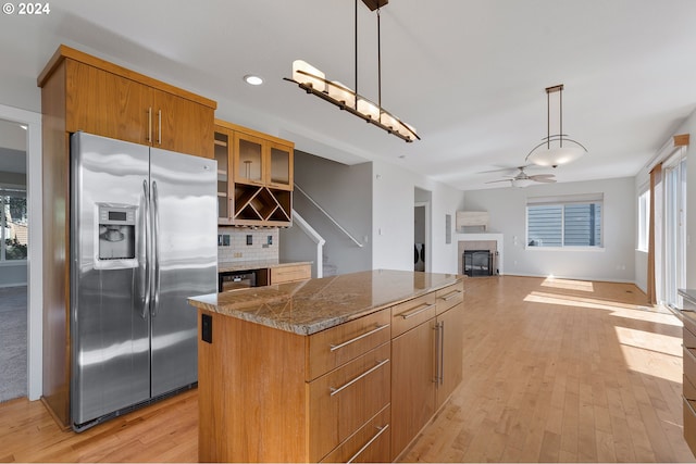 kitchen with decorative backsplash, hanging light fixtures, a kitchen island, light wood-type flooring, and stainless steel refrigerator with ice dispenser