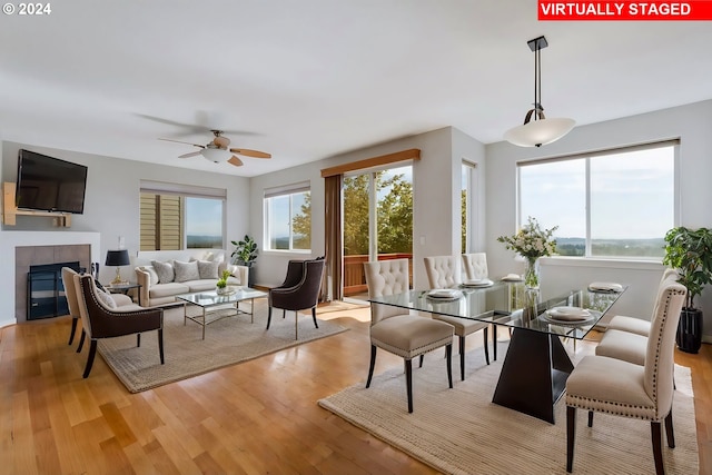 dining area featuring a water view, a tiled fireplace, light wood-type flooring, and ceiling fan