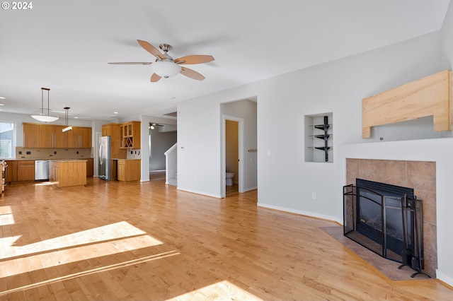 living room featuring a tiled fireplace, built in features, light wood-type flooring, and ceiling fan