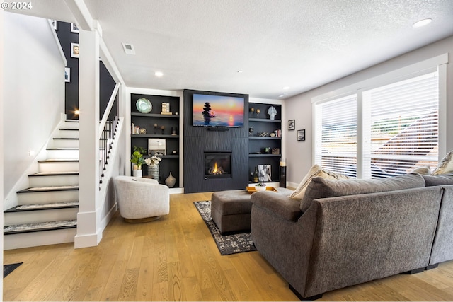 living room with a textured ceiling, built in features, a fireplace, and light hardwood / wood-style flooring