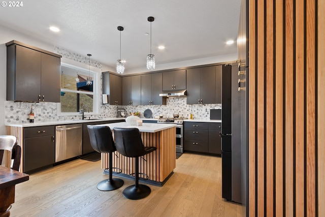 kitchen with appliances with stainless steel finishes, sink, decorative light fixtures, a center island, and a breakfast bar area