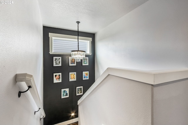 stairway featuring a textured ceiling and an inviting chandelier