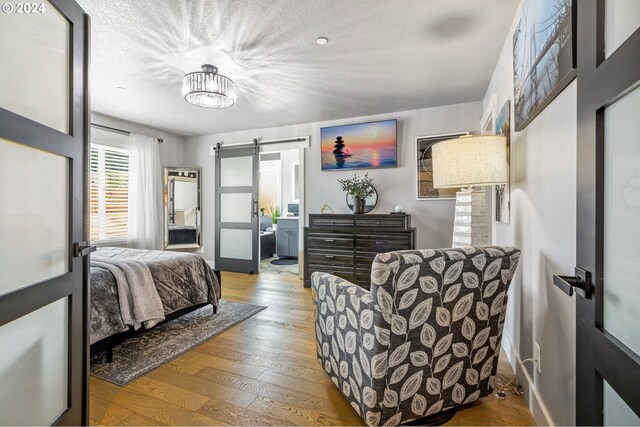 bedroom with ensuite bathroom, a textured ceiling, a barn door, a notable chandelier, and light hardwood / wood-style floors