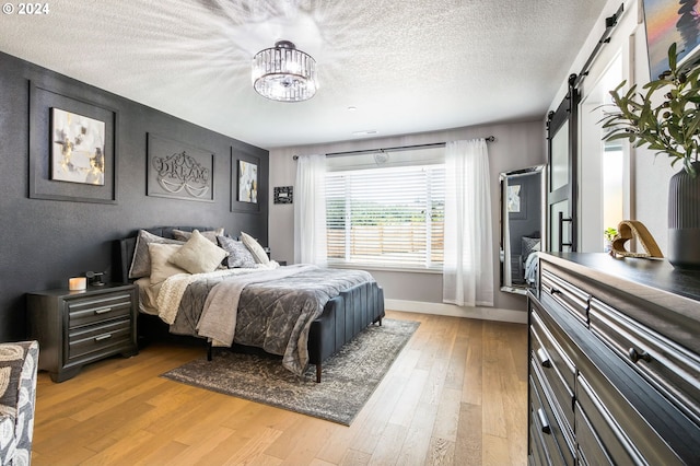 bedroom featuring a barn door, light hardwood / wood-style flooring, a textured ceiling, and a notable chandelier