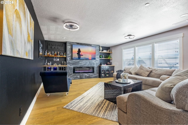 living room with hardwood / wood-style flooring, a textured ceiling, a high end fireplace, and bar area