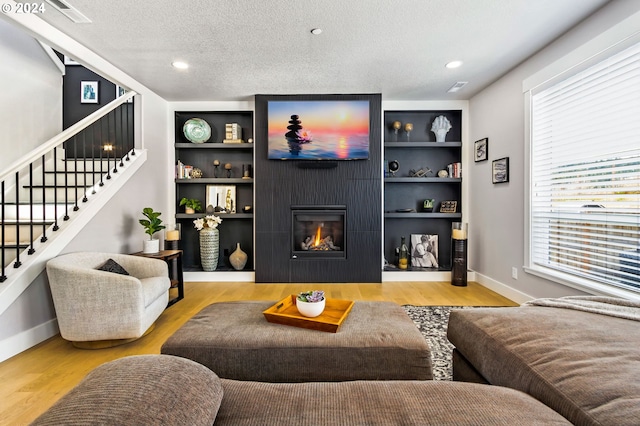 living room featuring a large fireplace, built in shelves, light hardwood / wood-style floors, and a textured ceiling