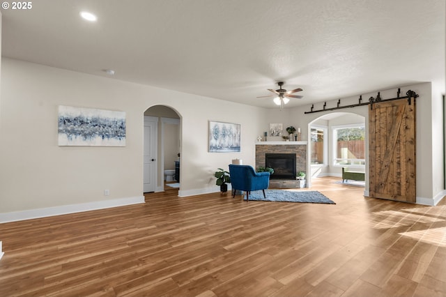 living area featuring light wood-style flooring, a ceiling fan, arched walkways, a stone fireplace, and baseboards