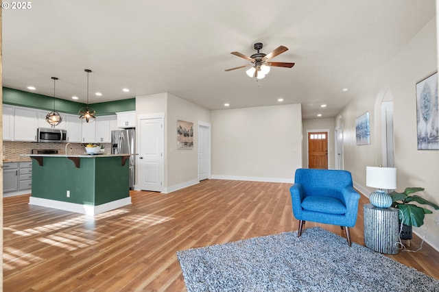 living area featuring light wood-type flooring, recessed lighting, arched walkways, baseboards, and ceiling fan