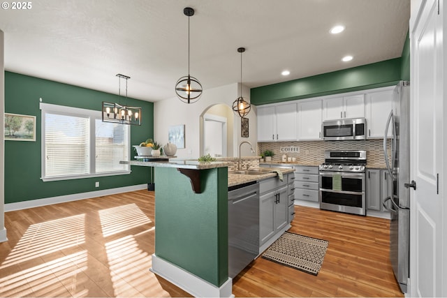 kitchen featuring light wood-type flooring, a sink, backsplash, stainless steel appliances, and arched walkways