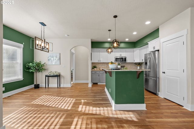 kitchen with a breakfast bar area, decorative backsplash, stainless steel appliances, arched walkways, and white cabinetry