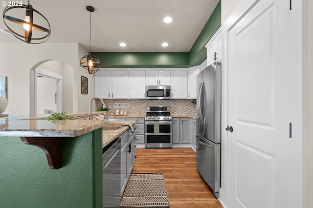 kitchen with light stone counters, light wood finished floors, a sink, appliances with stainless steel finishes, and a kitchen breakfast bar