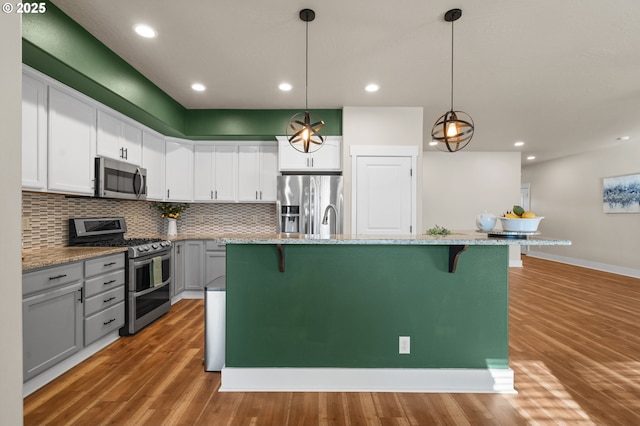 kitchen with a kitchen breakfast bar, backsplash, wood finished floors, and appliances with stainless steel finishes