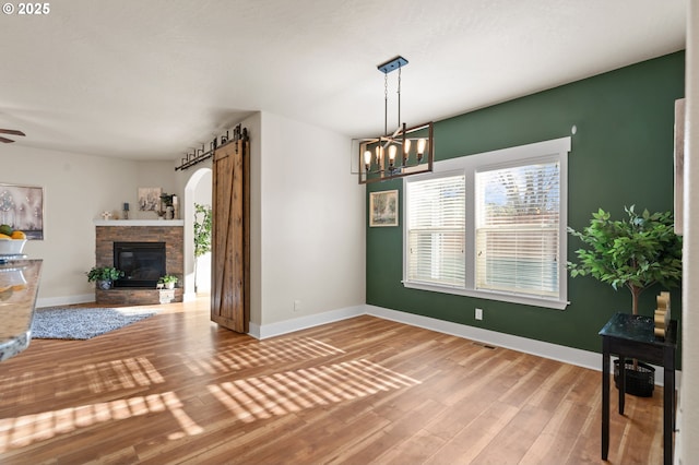 unfurnished dining area featuring baseboards, arched walkways, wood finished floors, and a fireplace