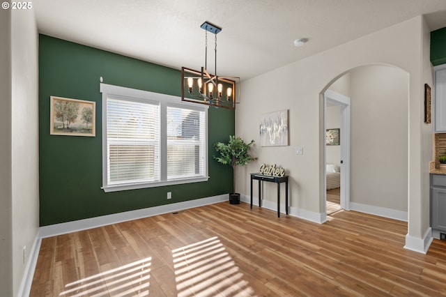 unfurnished dining area with a notable chandelier, wood finished floors, arched walkways, and baseboards