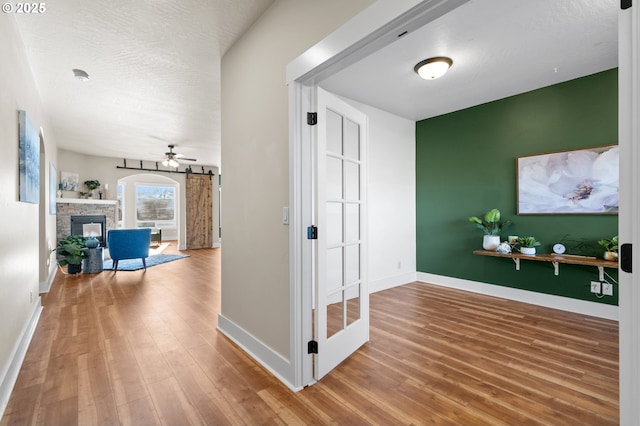 corridor featuring a barn door, baseboards, a textured ceiling, and wood finished floors