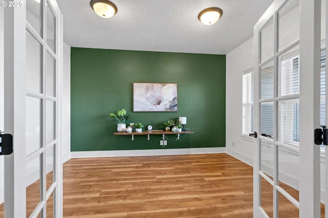 interior space with french doors, baseboards, an accent wall, and light wood finished floors