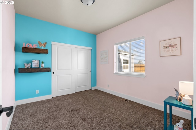 unfurnished bedroom with a closet, baseboards, visible vents, and dark colored carpet