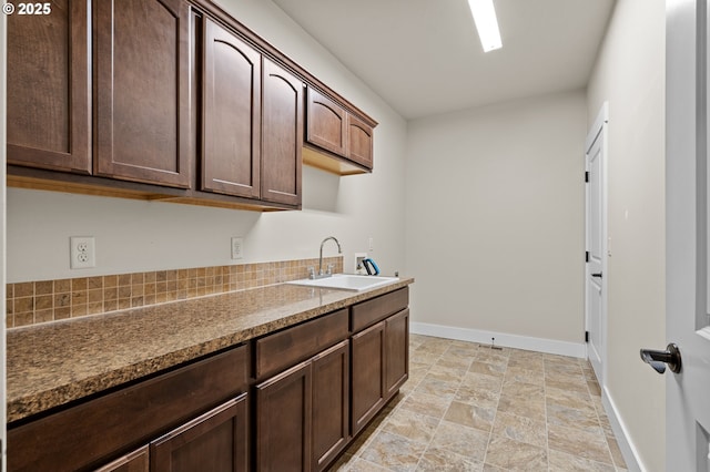 kitchen featuring a sink, stone finish flooring, baseboards, and dark brown cabinets