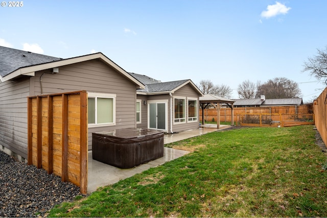 rear view of property featuring a hot tub, a gazebo, a lawn, a fenced backyard, and a patio