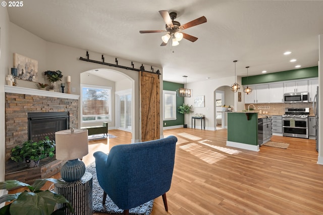 living area with a fireplace, arched walkways, ceiling fan, light wood-style floors, and a barn door