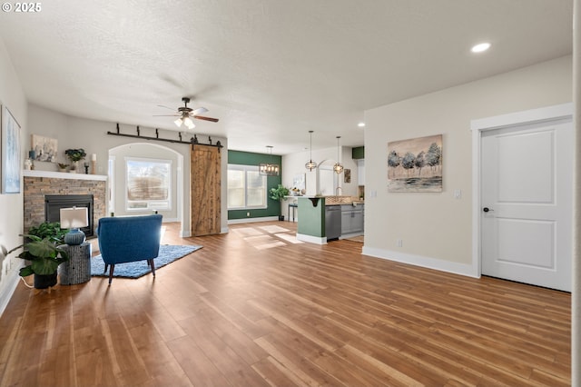 unfurnished living room with ceiling fan with notable chandelier, a barn door, a fireplace, light wood finished floors, and baseboards