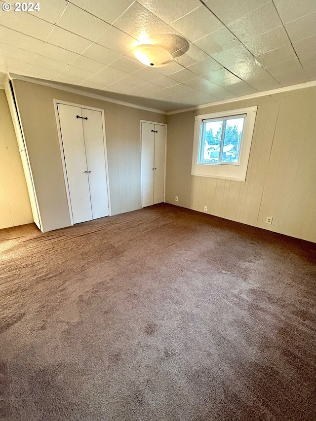 unfurnished bedroom featuring two closets, wooden walls, a paneled ceiling, and carpet