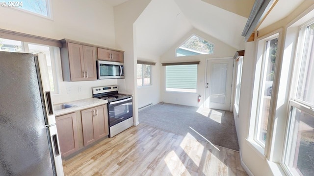 kitchen with a baseboard radiator, light wood-type flooring, vaulted ceiling, and stainless steel appliances