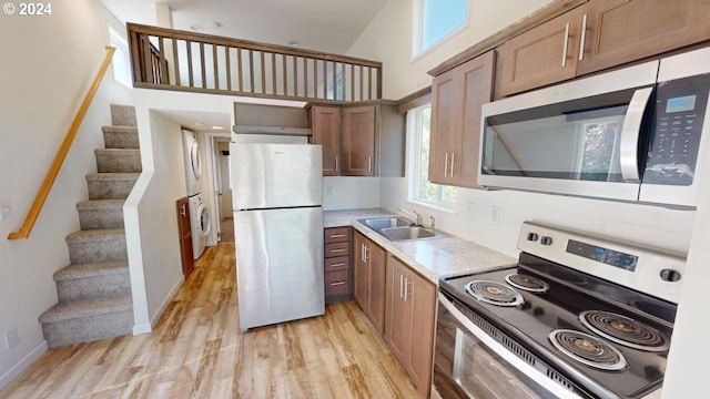 kitchen with a towering ceiling, light hardwood / wood-style floors, sink, stacked washer and clothes dryer, and stainless steel appliances