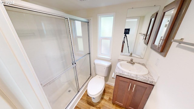 bathroom featuring wood-type flooring, a shower with door, toilet, and vanity