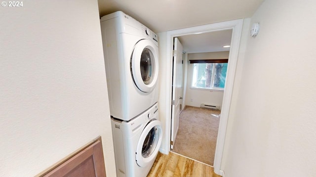 clothes washing area with light hardwood / wood-style floors, a baseboard radiator, and stacked washer / drying machine