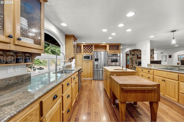 kitchen featuring a textured ceiling, decorative light fixtures, appliances with stainless steel finishes, light hardwood / wood-style floors, and sink