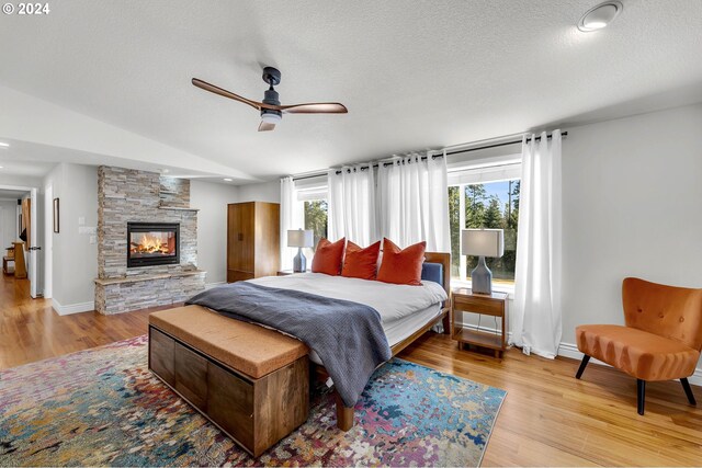 bedroom with ceiling fan, light hardwood / wood-style floors, a textured ceiling, and a stone fireplace