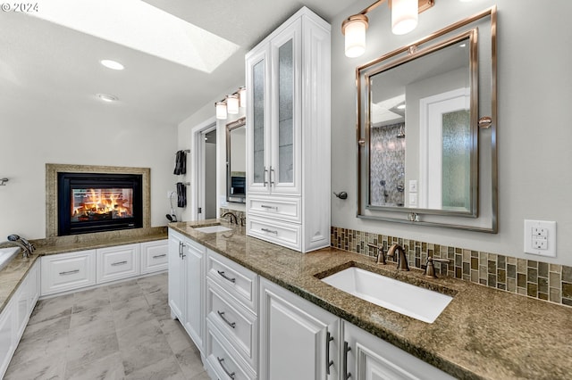 bathroom featuring a multi sided fireplace, backsplash, a tub to relax in, and vanity