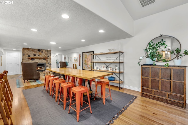 dining space featuring a textured ceiling, a stone fireplace, and light hardwood / wood-style floors