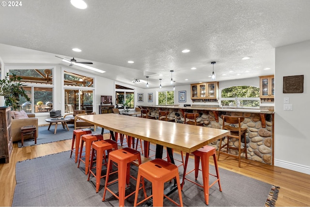 dining area with ceiling fan, hardwood / wood-style flooring, a textured ceiling, and vaulted ceiling