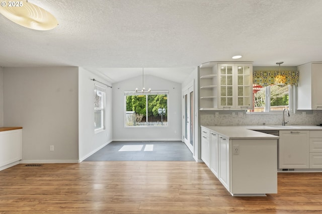 kitchen with an inviting chandelier, open shelves, a sink, vaulted ceiling, and light wood-style floors