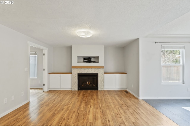 unfurnished living room featuring light wood-type flooring, baseboards, a textured ceiling, and a tile fireplace