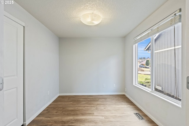 unfurnished room with visible vents, baseboards, a textured ceiling, and wood finished floors