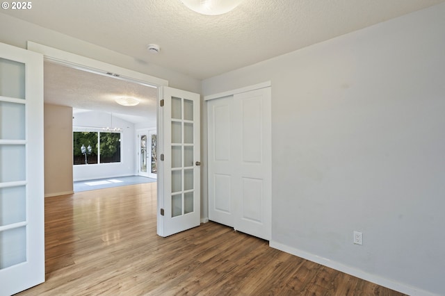 unfurnished room with french doors, a textured ceiling, baseboards, and wood finished floors