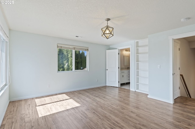 spare room with baseboards, light wood finished floors, and a textured ceiling